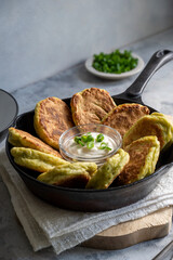 Zucchini fritters or pancakes in fryling pan with fresh herbs and sour cream.