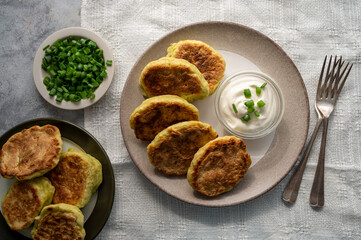 Zucchini fritters, stack of vegetarian zucchini pancakes in a plate, with fresh herbs and sour cream.