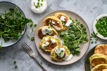 Zucchini fritters, stack of vegetarian zucchini pancakes in a plate, with fresh herbs and sour cream.