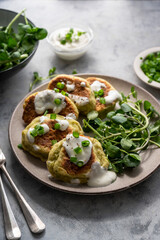 Zucchini fritters, stack of vegetarian zucchini pancakes in a plate, with fresh herbs and sour cream.