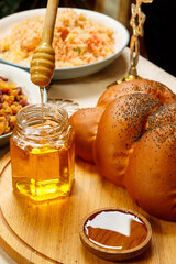 Honey drips from a wooden spoon into a jar next to the menorah challah and couscous.