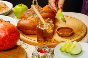 A woman's hand dips an apple in honey at a meal at the festive table in honor of Rosh Hashanah.