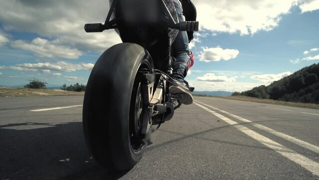 Close up of a stunt biker on a motor bike on road with smoke of the tire