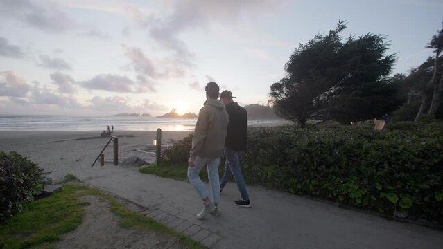 
Two guy friends walk down to tofino beach during sunset
