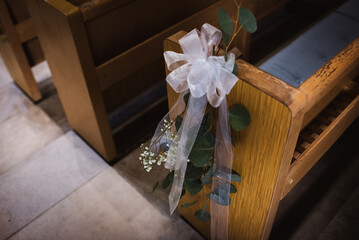 Wedding bow and florals draped over end of Church pew for ceremony