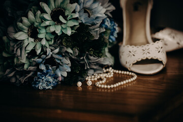 Pearl necklace and earrings strewn in front of pair of wedding heels with blue bouquet 