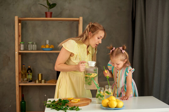 mom pours lemonade into glasses, and daughter puts tubes in a glass. drink fresh lemon juice in kitchen
