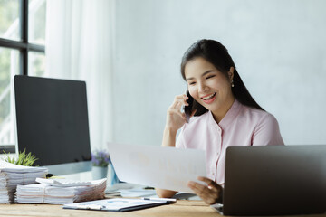 Beautiful Asian woman talking on the phone in the office of a startup company, she is a company finance employee working in the finance department. Concept of women working in a company.