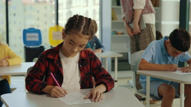 Caucasian brunette school girl is doing test thinking about answers in the classroom. Elementary school. Learning and education concept.