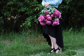 a beautiful woman in a black dress standing and holding a bouquet of pink flowers in the countryside in front of green trees, nature around