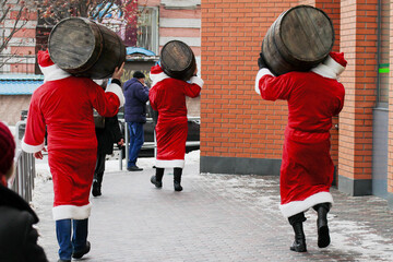 Three Santa Clauses carry a wooden keg of beer