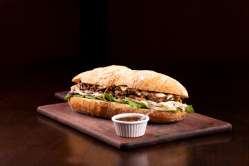 fast food beef brisket sandwich with arugula and coleslaw salad on baguette bread on wooden board...