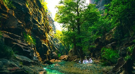 People camping in a narrow valley surrounded by trees and river flowing in the middle. An image from Wadi Lajab, Saudi Arabia