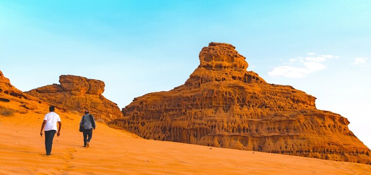 People hiking in desert surrounded by sandstone formations. An image from Al Ula, Saudi Arabia