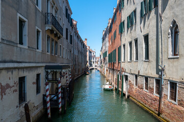 Fototapeta na wymiar Vue typique d'un canal a Venise avec les reflets, les bateaux et un pont sur fond de ciel bleu