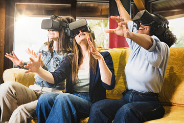 Three young women sitting on the couch having fun playing a metaverse game wearing 3d googles for...