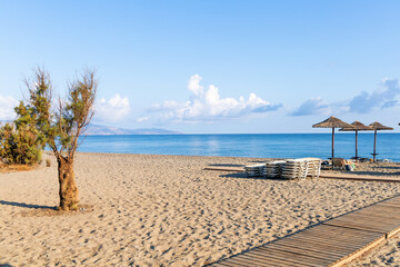 Empty beach with sun loungers and umbrellas in the early morning on a sunny day on the Crete island...