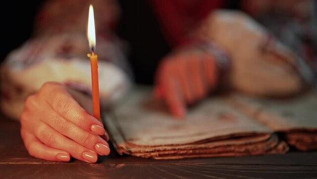 Ukrainian woman reading ancient book - Bible. Concentrated attentively follows finger on paper page under candle light. History of Kyiv Rus. Psalter, 19th century, prayers and psalms