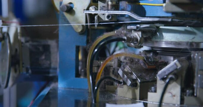 White thread stretched in a weaving loom, working sewing machine. One of the stages of machine production of clothing at a garment factory. Robotization of labor.