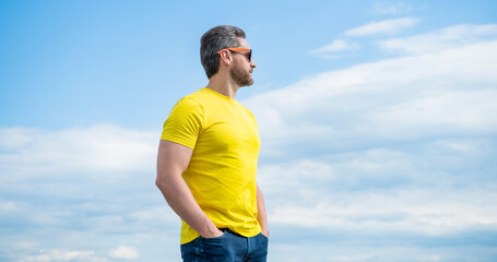 bearded man in yellow shirt and sunglasses outdoor on sky background