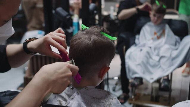 Fashionable hairdresser cuts a child's hair with a clipper in a barbershop. Close up side view portrait Men's hairstyle and haircut in the salon.