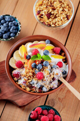 Yogurt with granola, fruits and berries on a clay plate with a wooden spoon. Yogurt with granola and fruits on wooden boards. Top view