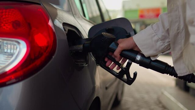 Refueling a car with fuel, Filling fuel into a car tank. Girl driver refuels auto gas station for cars. The car's tank cap is open. Hand holding faucet atomizer for refueling

