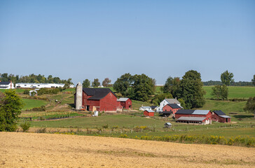 Fototapeta na wymiar Amish farm in a valley surrounded by fields and trees in the farmland countryside of Holmes County, Ohio