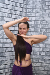 A beautiful dancer in oriental attire poses in a dance style in the studio against a brick wall