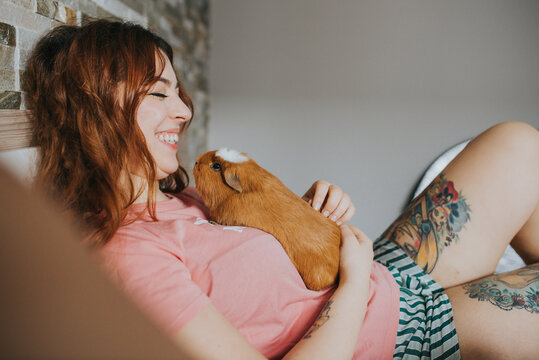 Woman With Guinea Pig Resting On Bed
