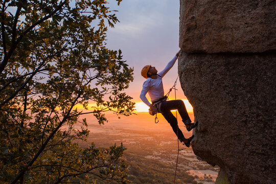 Skilled climber hanging on mountain while holding hand above green valley