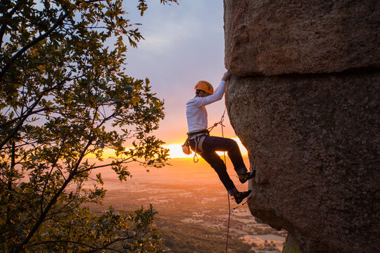Skilled climber hanging on mountain while holding hand above green valley