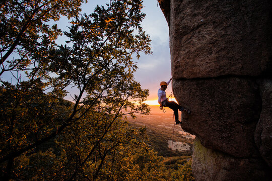 Skilled climber hanging on mountain while holding hand above green valley
