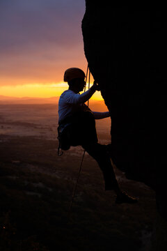 Skilled climber hanging on mountain while holding hand above green valley