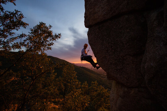 Skilled climber hanging on mountain while holding hand above gre
