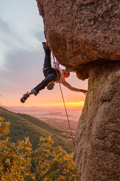 Skilled climber hanging on mountain while holding hand above green valley