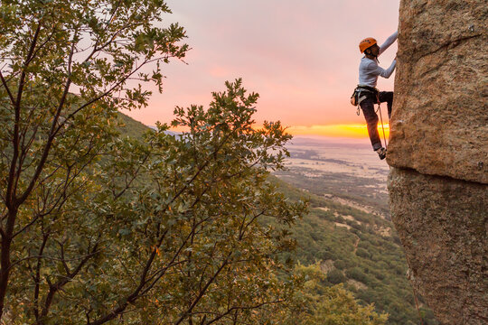 Skilled climber hanging on mountain while holding hand above green valley