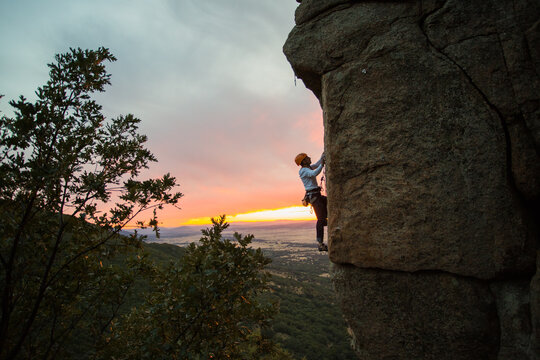 Skilled climber hanging on mountain while holding hand above green valley