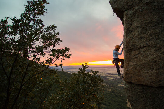 Skilled climber hanging on mountain while holding hand above green valley
