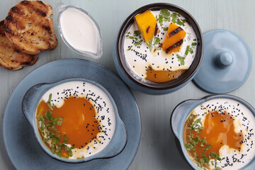 Hot creamy pumpkin puree soup with cream, black cumin seeds, herbs and toasted bread on a blue wooden table