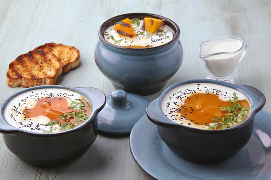 Hot creamy pumpkin gazpacho with cream, black cumin seeds, herbs and toasted bread on a blue wooden table