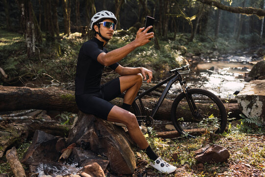 Unrecognizable cyclist taking photo of river on smartphone in forest
