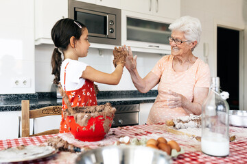 Happy girl with grandmother giving high five in kitchen