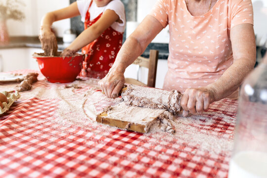 Anonymous grandmother and girl preparing dough at home
