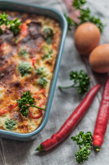 Baking dish with casserole, eggs, chili pepper and curly parsley.
