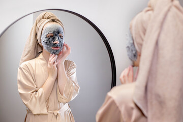 Young well-groomed woman applies a mask to cleanse and moisturize the face. Cosmetic procedures,...