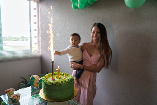 Happy ethnic with son standing near cake with burning firework