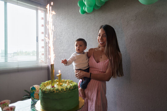Happy ethnic with son standing near cake with burning firework