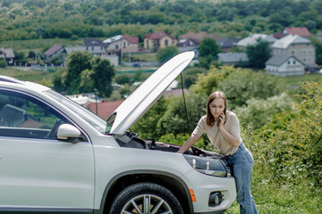 Young woman opening bonnet of broken down car having trouble with her vehicle. Worried woman talking on the phone near broken car.