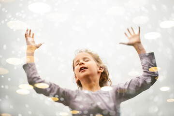Blond girl child joyfully raises hands in air with light bokeh
